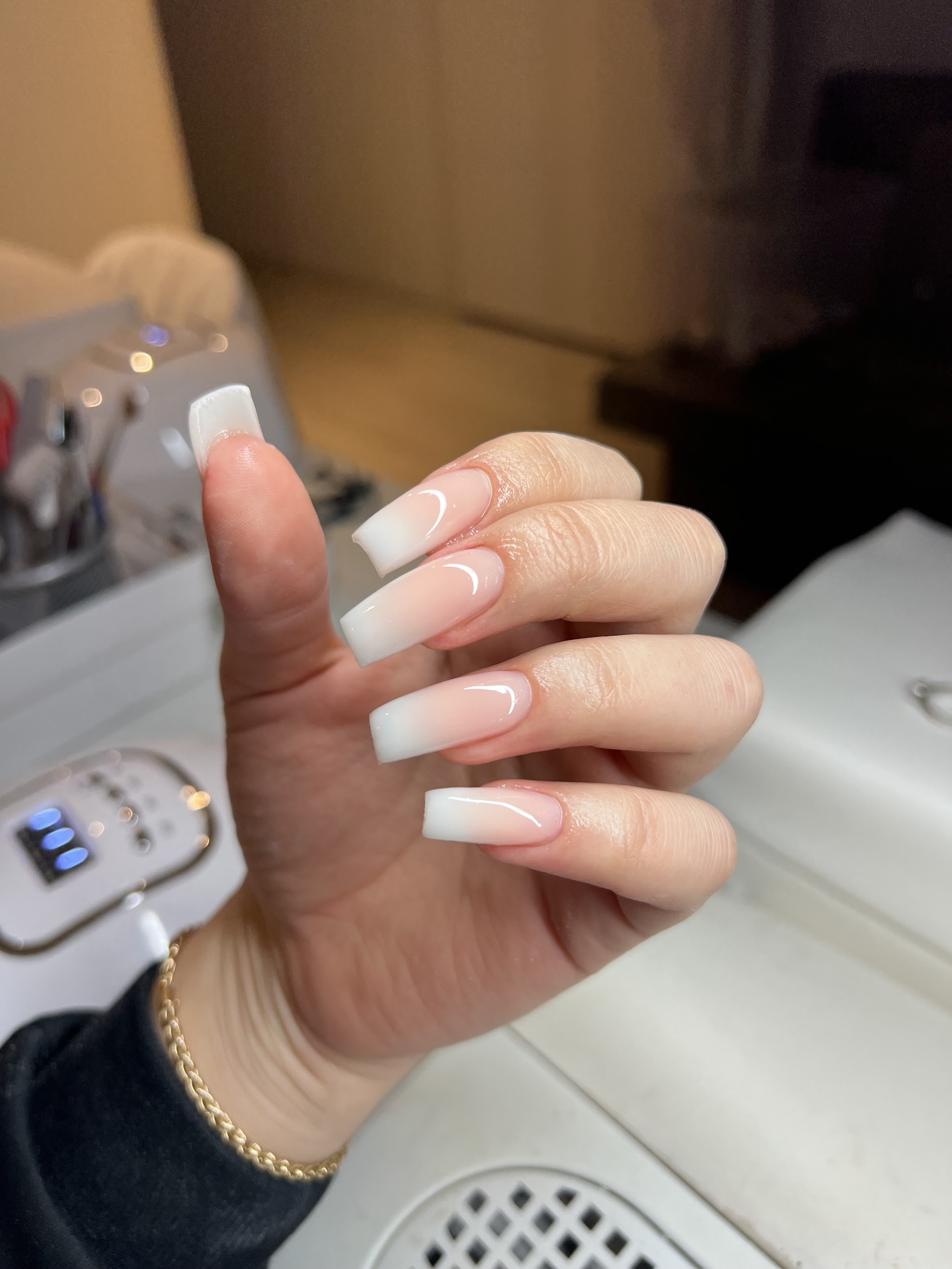 Witte ombre coffin nagels aan de werktafel in de studio, met de UV-lamp op de achtergrond